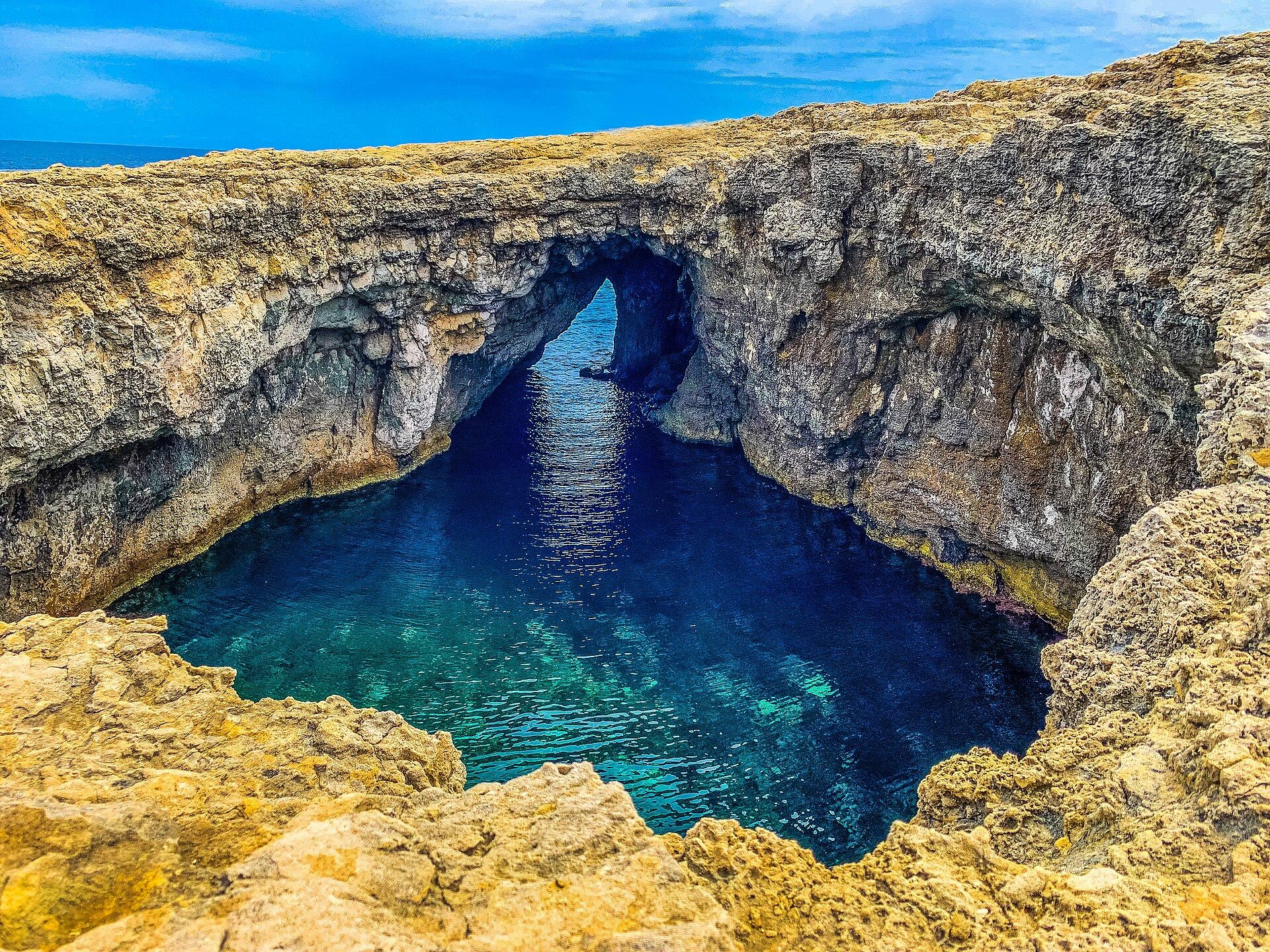 The collapsed sea cave at Coral Lagoon — a deep blue pool enclosed by rock, open to the sky, with an arch to the sea
