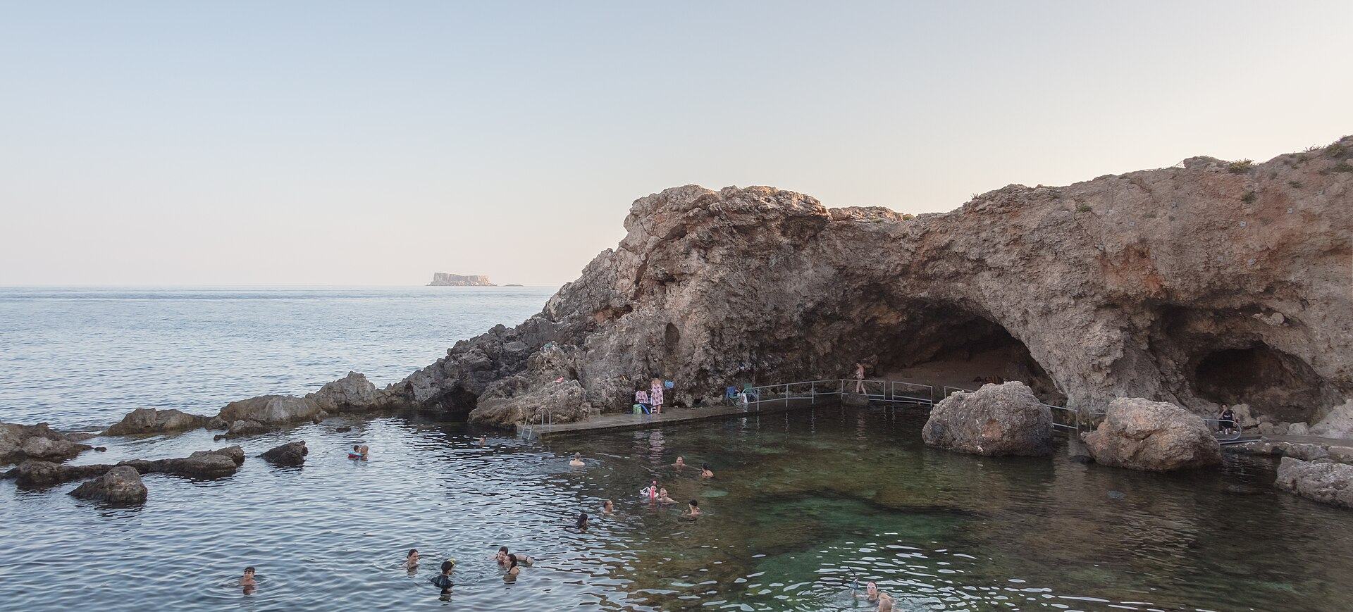 The sheltered rock pool at Għar Lapsi under the Siġġiewi cliffs, with swimmers and the islet of Filfla on the horizon