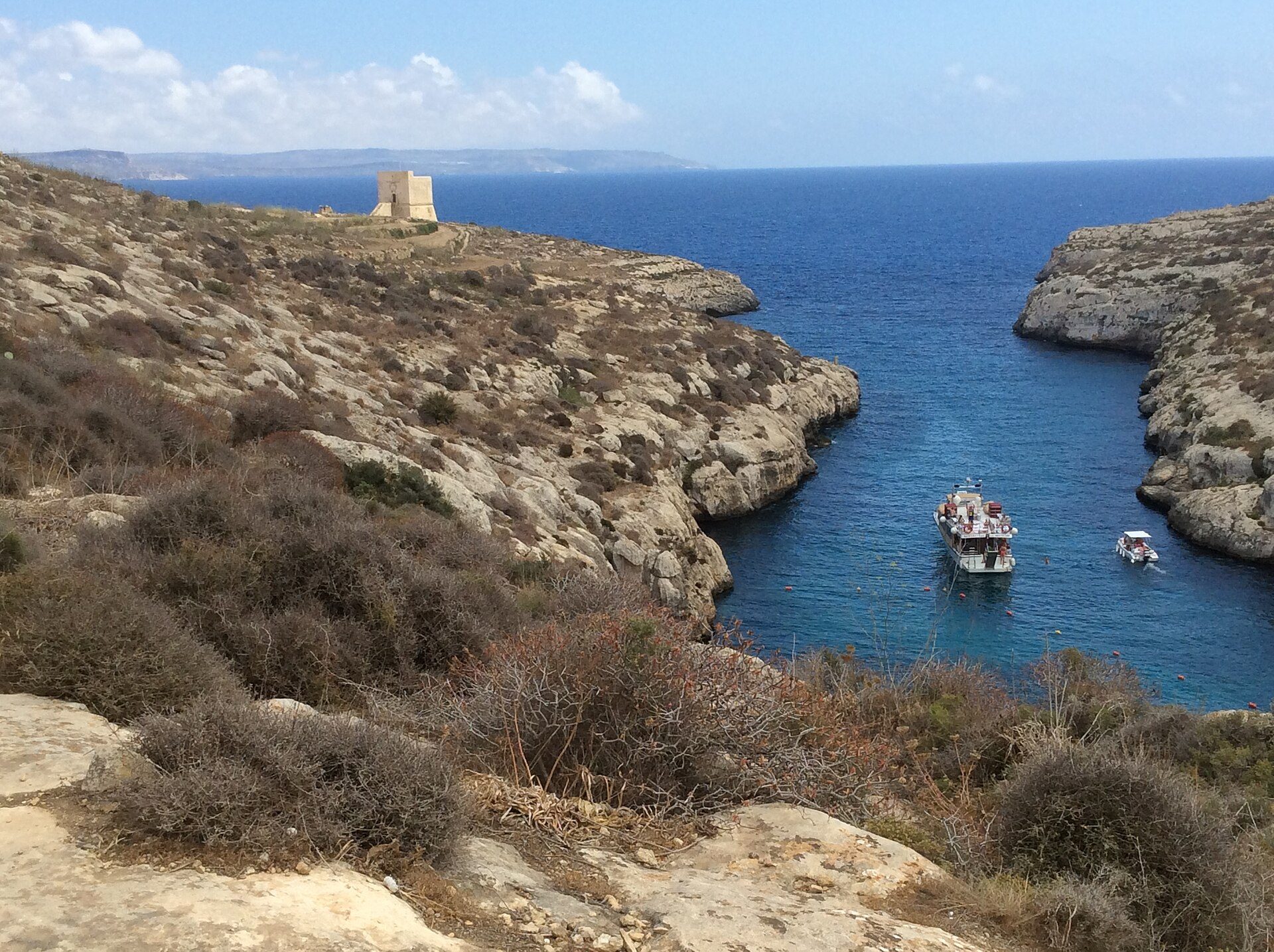 The narrow creek at Mġarr ix-Xini seen from above, with boats moored in it and the Knights' watchtower on the headland