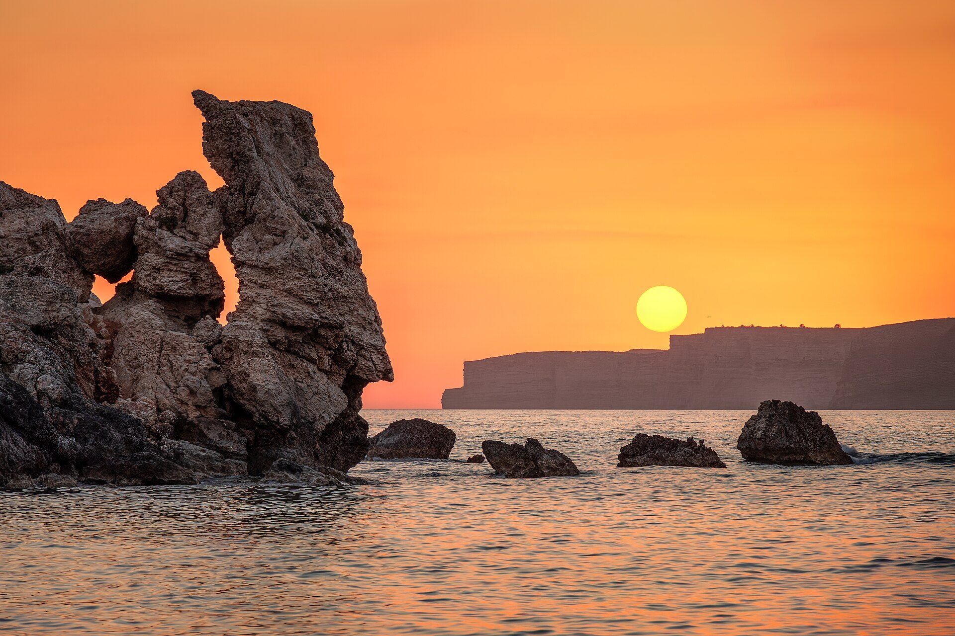 Sea stacks silhouetted against an orange sky as the sun drops to the horizon off the Maltese coast